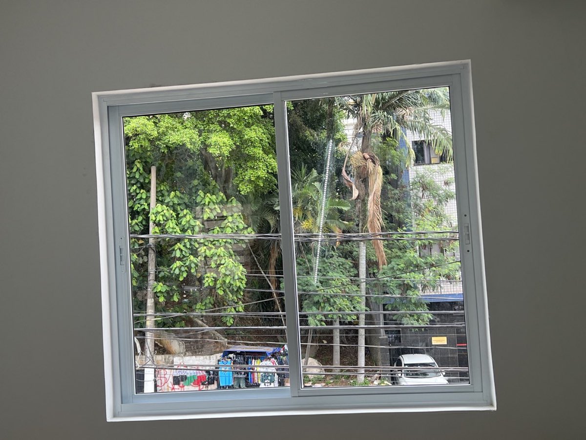 Janela ampla de alumínio branco com grade de proteção e vista para a rua.
