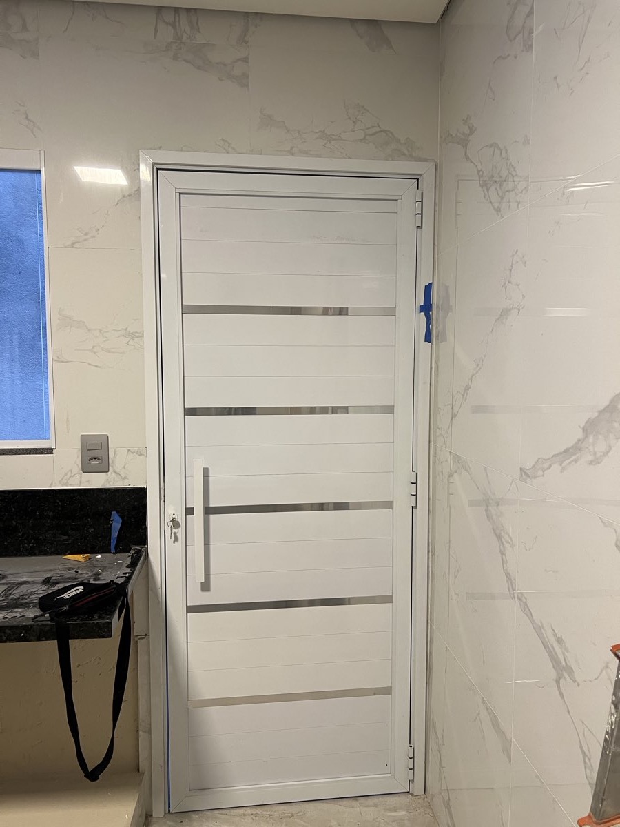 Porta de alumínio branco com frisos horizontais em aço inox, instalada em ambiente revestido de mármore.