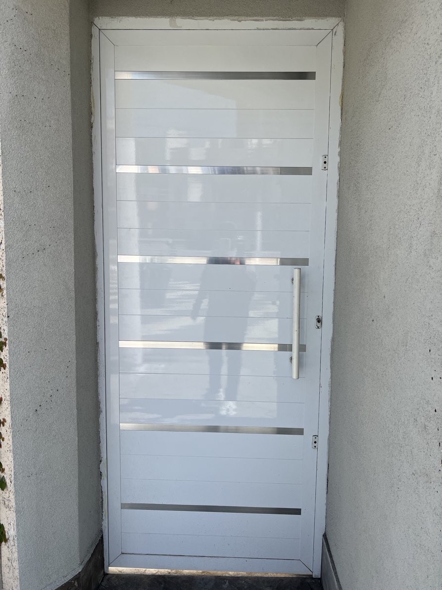 Porta de entrada em alumínio branco com frisos em aço inox e puxador tubular.