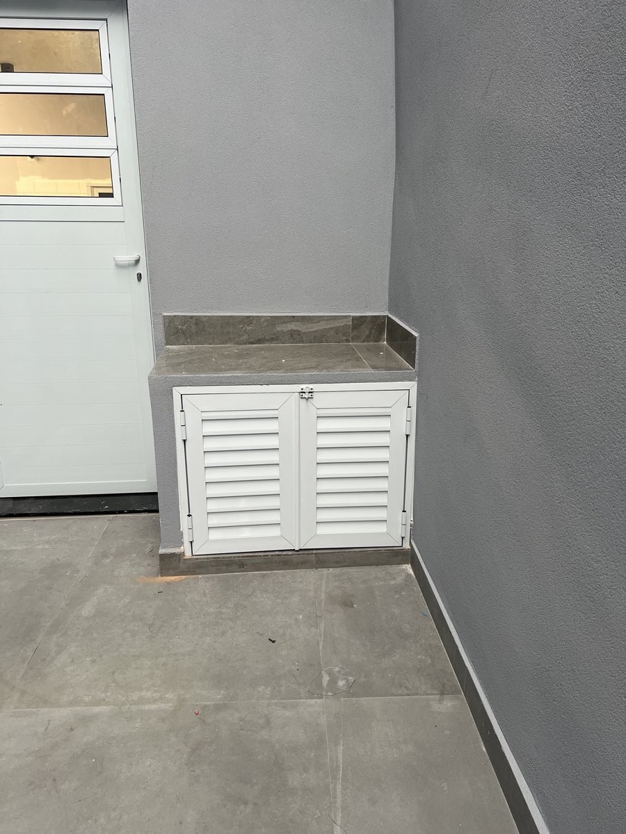 Abrigo de pia em alumínio branco com portas em veneziana, instalado em área de serviço externa.
