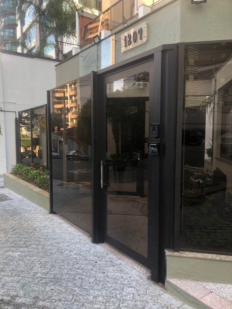 Entrada de edifício envidraçada com esquadrias de alumínio preto.