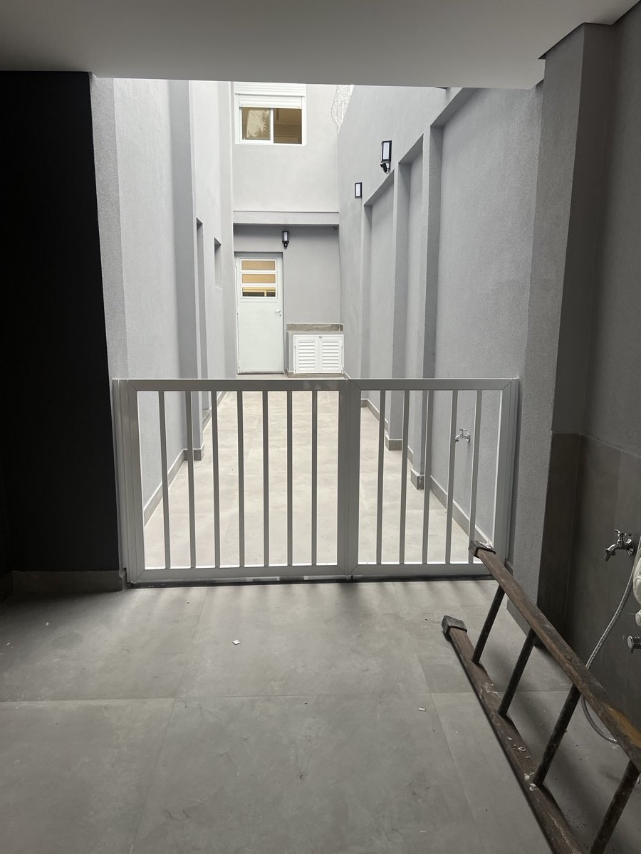 Portão de duas folhas em alumínio com gradil vertical, dando acesso a corredor externo.