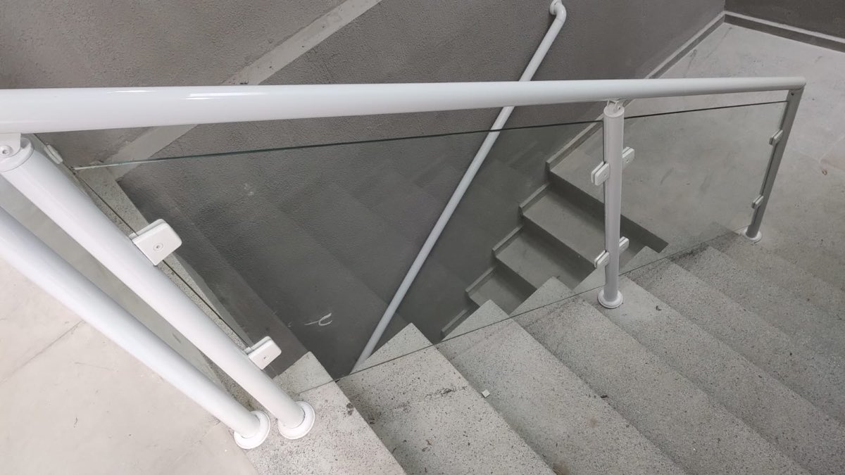 Guarda-corpo de vidro temperado com montantes e corrimão em alumínio branco, instalado em escada.