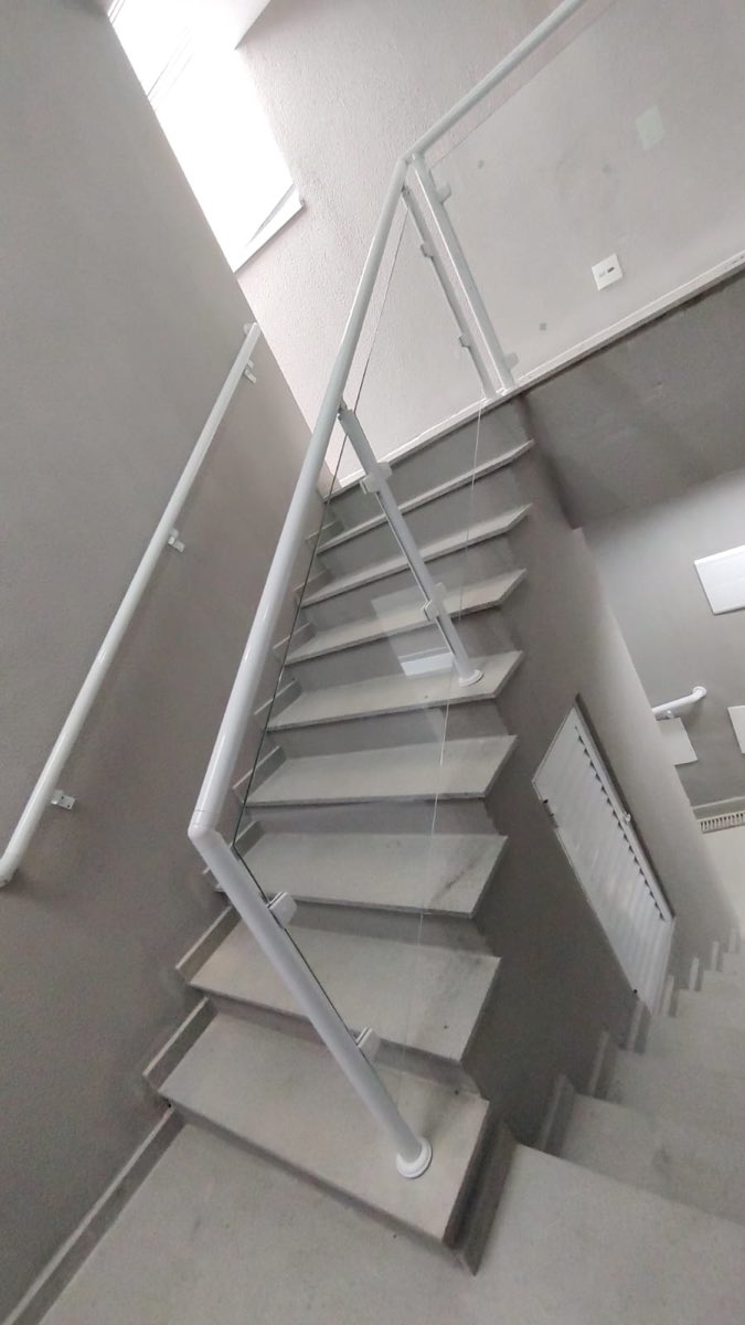 Escada com guarda-corpo de vidro temperado e corrimão em alumínio branco acompanhando os degraus.