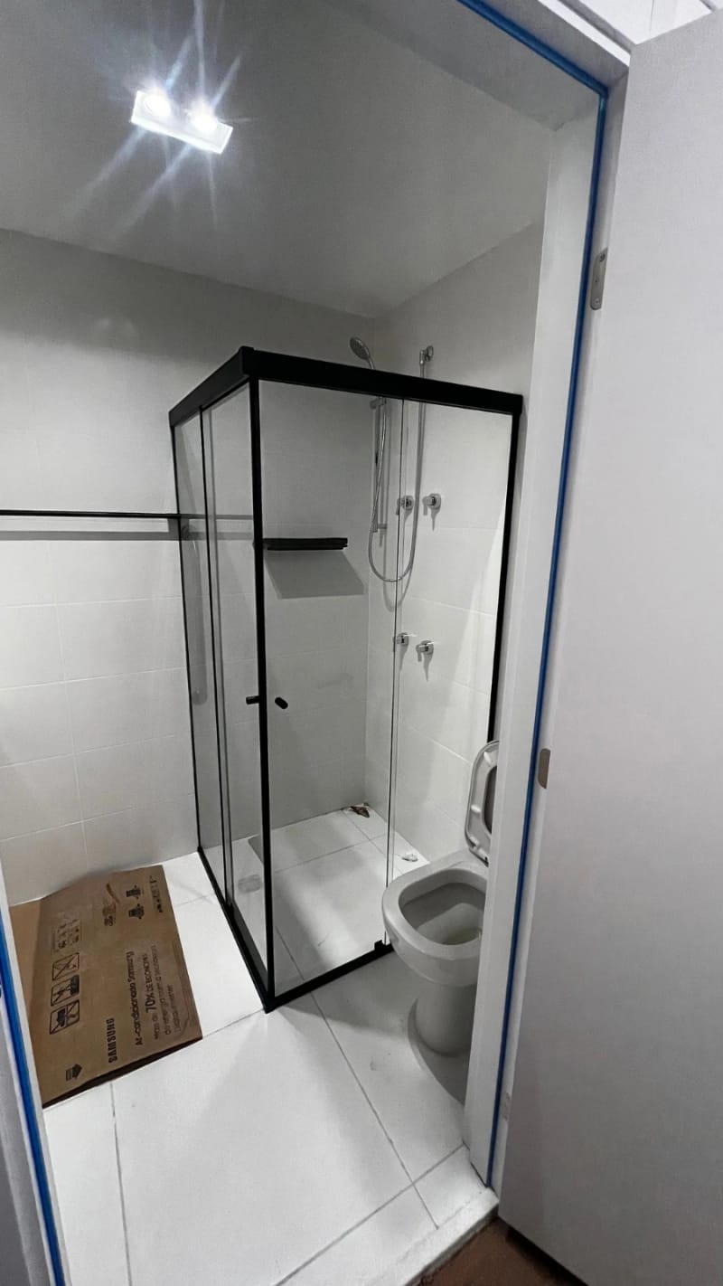 Box de canto em vidro incolor com perfil preto, recém-instalado em banheiro de apartamento novo.