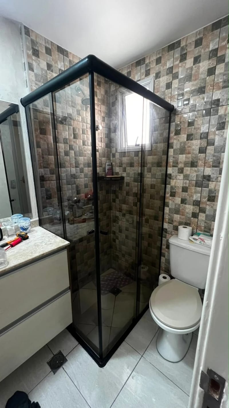 Box de canto em vidro fumê com perfil de alumínio preto, instalado em banheiro com revestimento de pastilhas.