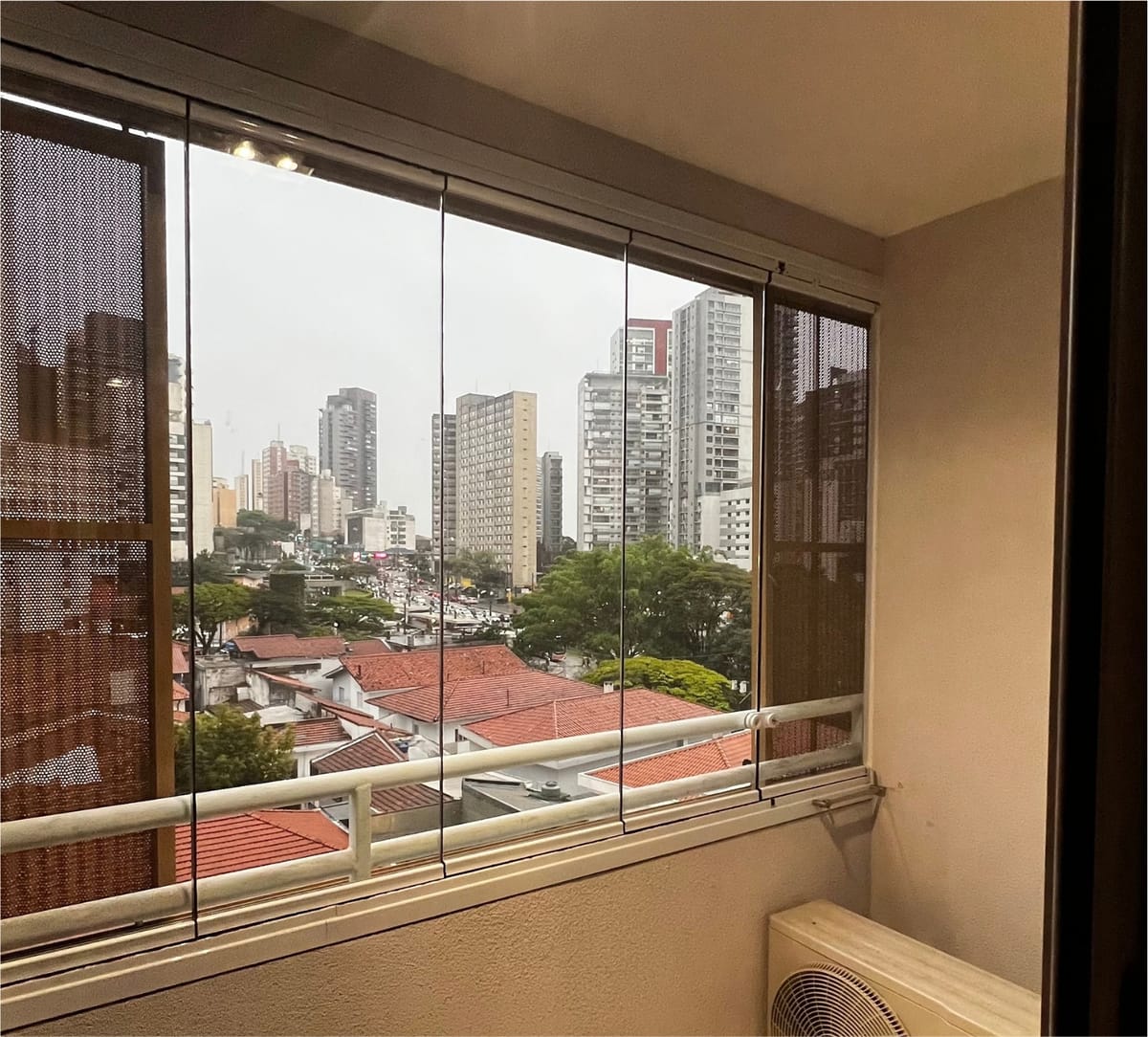 Varanda de apartamento fechada com vidro retrátil, com vista para os prédios e casas da Vila Madalena. Obra da VitraAlu em Vila Madalena, São Paulo.